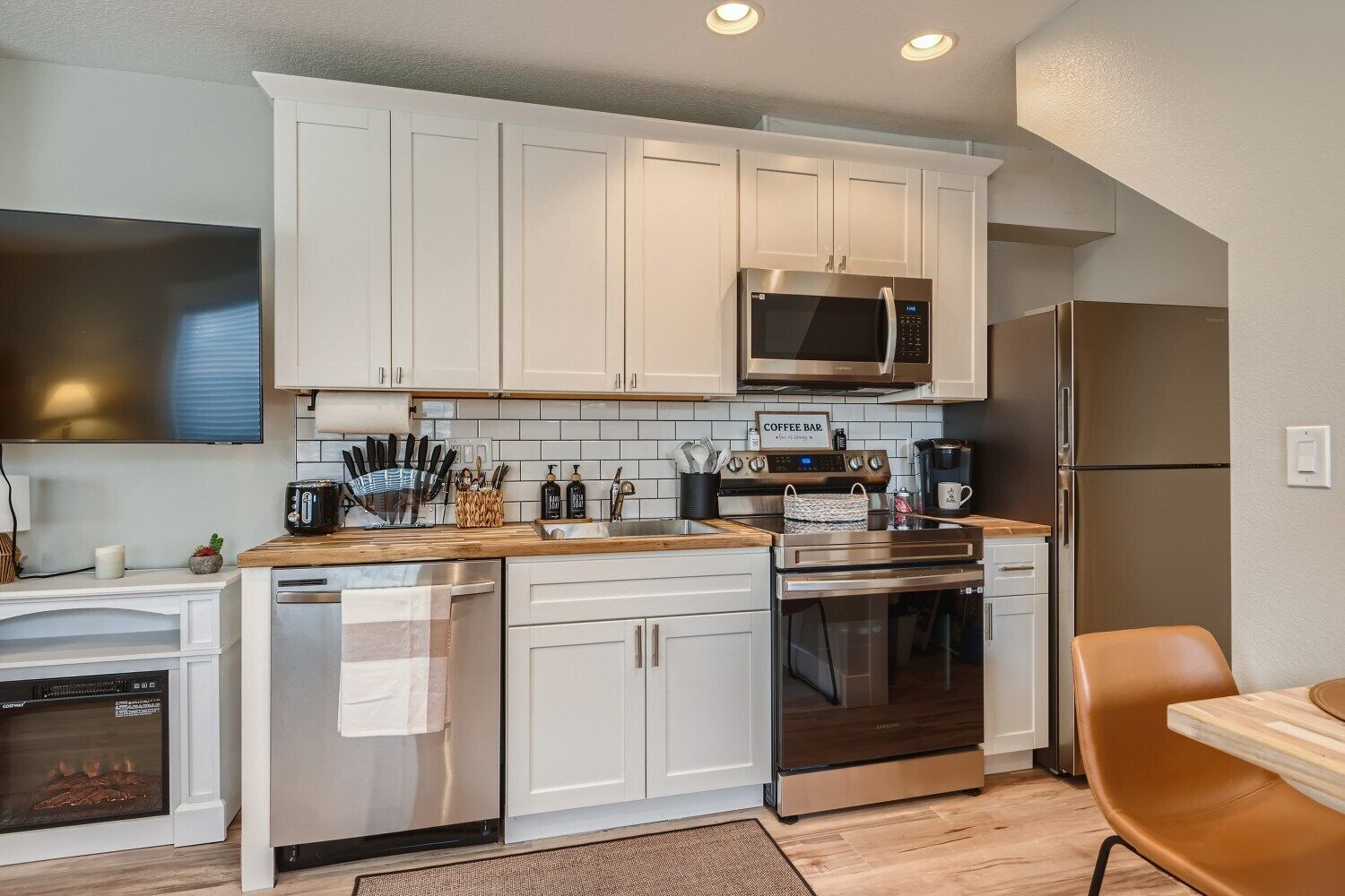 A modern kitchen with white cabinets, stainless steel appliances, and a wooden countertop.