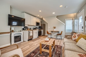 A modern kitchen with white cabinets, a flat-screen TV, and a dining area with a wooden table and two chairs.