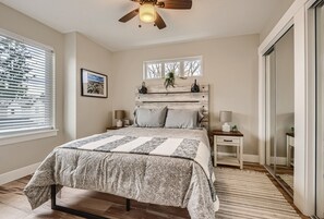 A bedroom with a bed, bedside tables, a ceiling fan, a window with blinds, a framed picture, and a mirror.