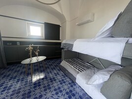 Una habitación compacta con una cama litera, una mesita con un florero y una zona de kitchenette.