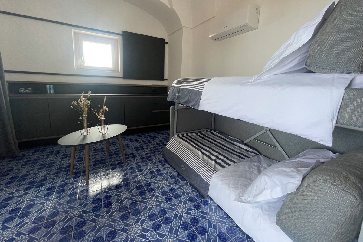 Een kleine kamer met een stapelbed, een tafeltje met een vaas en een kitchenette.