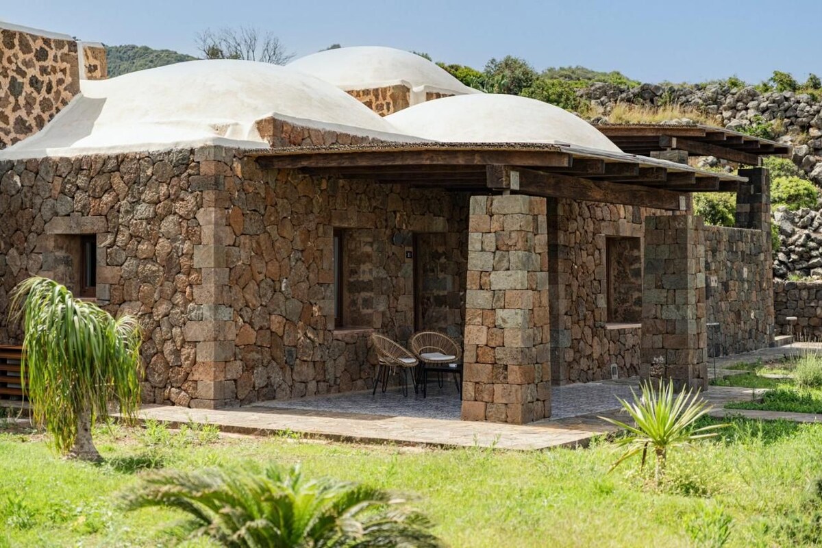 A stone building with a covered patio area and two wicker chairs.