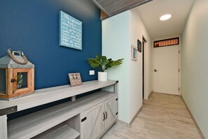 A hallway with a blue wall, a wooden bench, a potted plant, and a door at the end. - Charming Kihei Oasis Vistas  (Kihei)