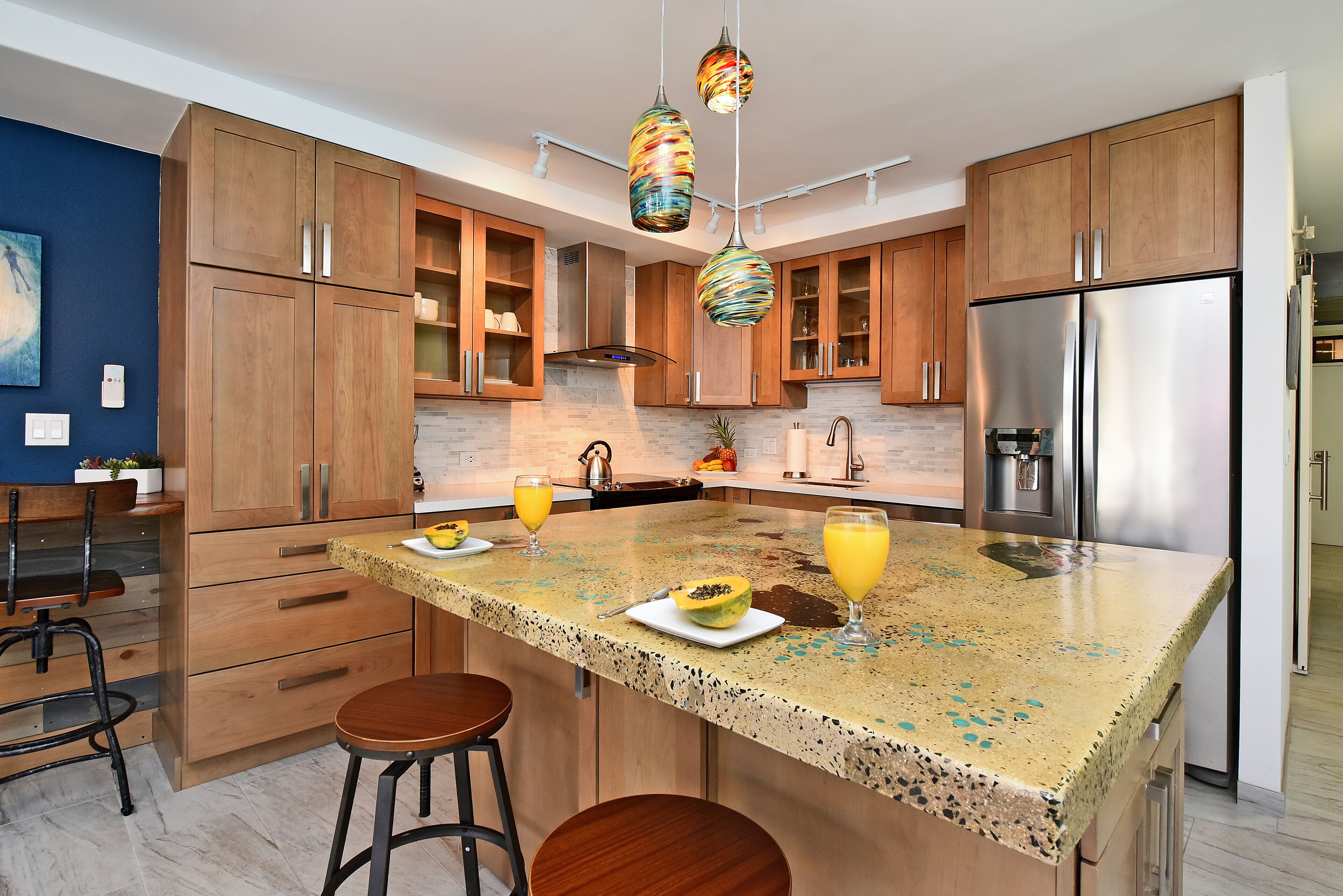 A modern kitchen with wooden cabinets, a granite countertop, stainless steel appliances, and colorful pendant lights.