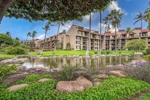 A hotel with multiple balconies, a landscaped garden with a pond, and palm trees. - Charming Kihei Oasis Vistas  (Kihei)