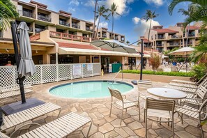 A poolside area with lounge chairs and umbrellas, surrounded by a pool and a building with balconies. - Charming Kihei Oasis Vistas  (Kihei)