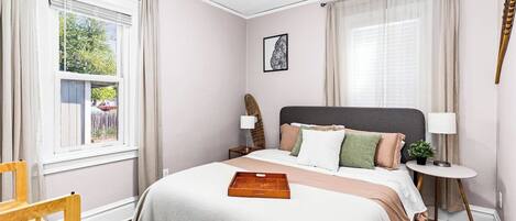 A bedroom with a bed, a bedside table, a chair, and a window.