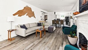 A modern living room with a sofa, coffee table, and chairs. A wooden map is on the wall, and there's a fireplace. - Light and Bright Northland (Superior)