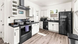 A modern kitchen with white cabinetry, black appliances, and a wooden floor. - Light and Bright Northland (Superior)