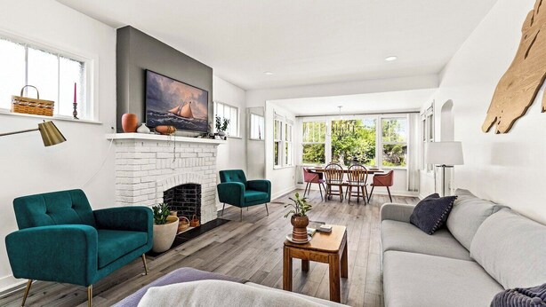 A spacious living room with a fireplace, teal armchairs, a grey sofa, and a dining area with a table and chairs. - Light and Bright Northland (Superior)
