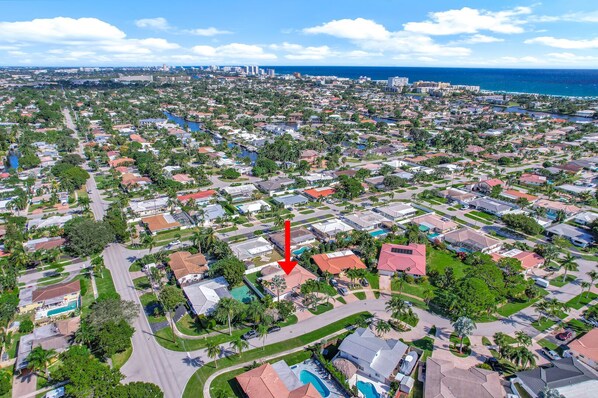 An aerial view of a residential area with a prominent red arrow pointing to a house with a swimming pool.