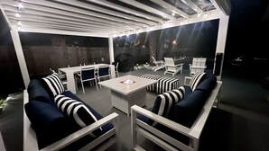 Eine Außenpatio-Terrasse mit weißen Möbeln, darunter Sofas und Stühle, und einem zentralen Tisch mit Feuerstelle.