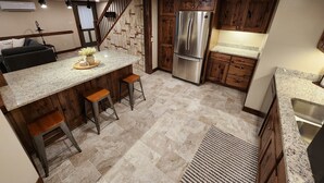 A kitchen with a granite countertop, wooden cabinets, a stainless steel refrigerator, and a built-in stove. - Gorgeous 5 bed Remodel near Downtown Hudson for Groups! (Hudson)