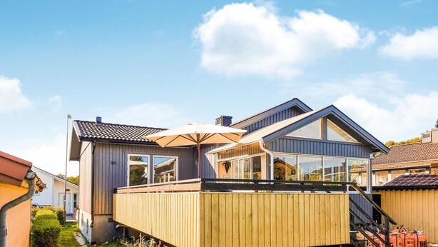 Una casa moderna con terraza de madera, ventanas grandes y cielo despejado.