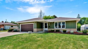 A single-story house with a garage, a covered front porch, and a well-maintained lawn. - Group Getaway Retreat: Hot tub, Game Room, Cinema & Firepit (Milwaukee)