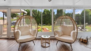 A room with two wicker chairs, a small round table, and large windows offering a view of a garden. - Group Getaway Retreat: Hot tub, Game Room, Cinema & Firepit (Milwaukee)