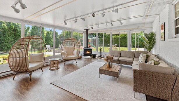 A spacious living room with a fireplace, wicker furniture, and large windows offering a view of the outdoors. - Group Getaway Retreat: Hot tub, Game Room, Cinema & Firepit (Milwaukee)