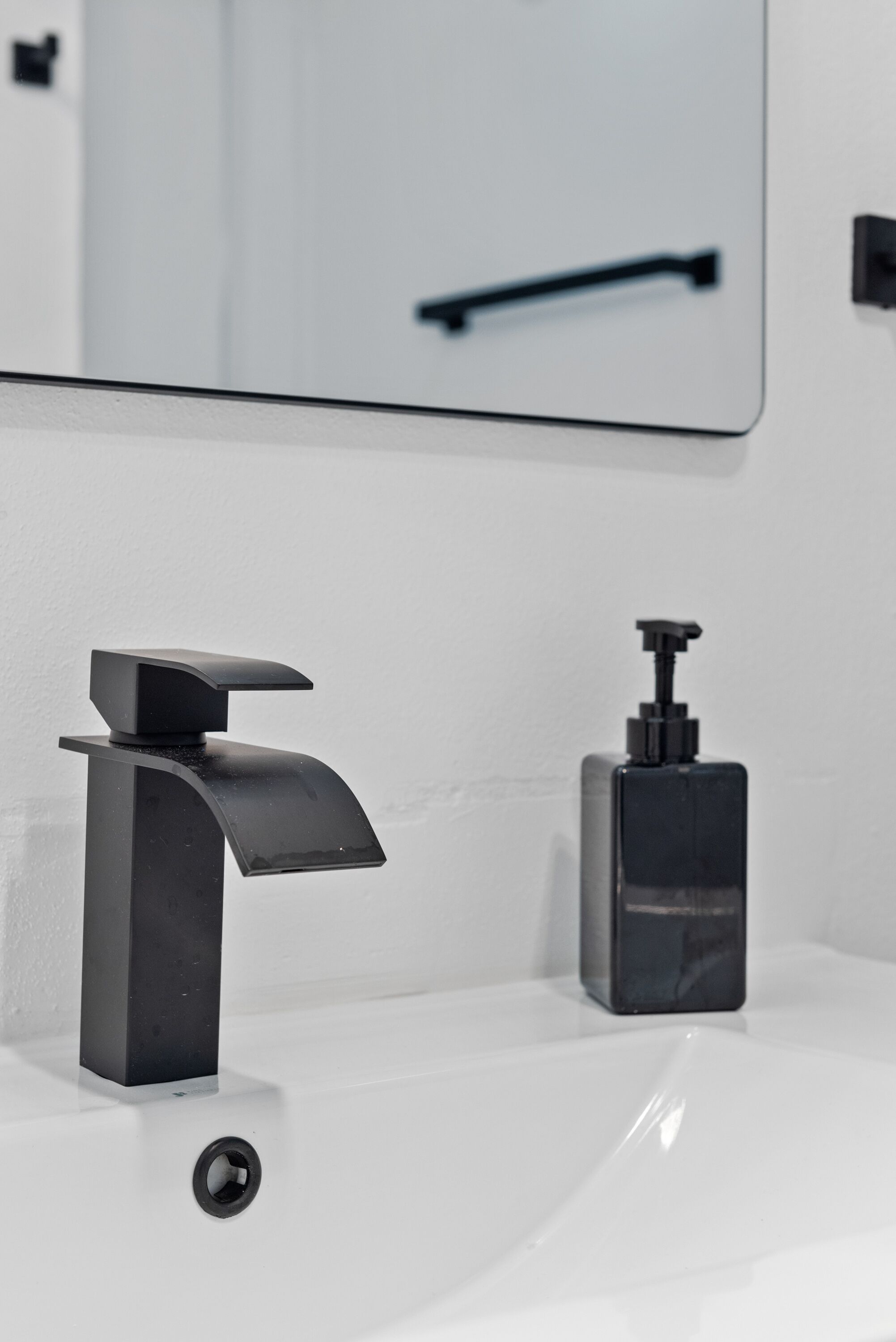 Un baño moderno con un grifo y dispensador de jabón negros sobre un lavabo blanco.
