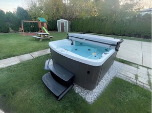 Een jacuzzi in een achtertuin, met een schommel en een tuinhuis op de achtergrond.