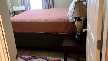A bedroom with a bed, a bedside table with a lamp, a rug, and a window with curtains.