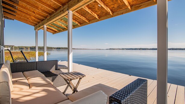 A covered outdoor seating area with a view of a calm lake and distant hills.
