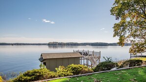 A lakeside view with a dock, a small building, and a grassy area.