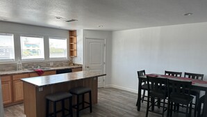 A modern kitchen with a central island, wooden cabinets, and a dining area with a table and chairs. - For your best vacation ever! (Crescent City)