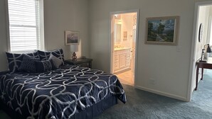 A bedroom with a large bed, a nightstand, a painting, and a door leading to a bathroom. - For your best vacation ever! (Crescent City)