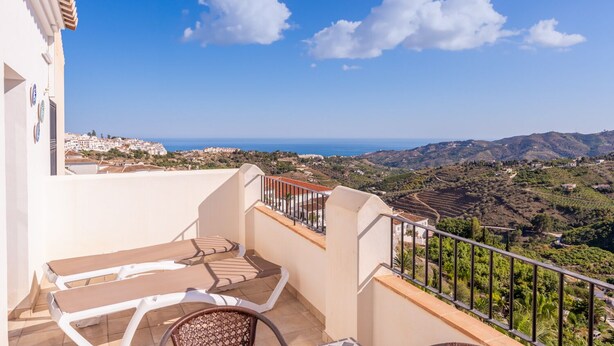 A balcony with a view of a coastal landscape, including hills and the sea.