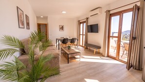 A spacious living room with a sofa, coffee table, and chairs, a flat-screen TV, and a sliding glass door leading to an outdoor area.