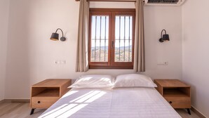 A bedroom with a bed, two nightstands, a window with curtains, and wall-mounted lights.