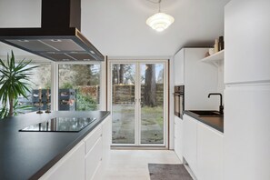 Een moderne keuken met een groot eiland, schuiframen naar een achtertuin en een hanglamp.