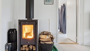 A room with a wood-burning stove, a stack of firewood, and a door leading to another room. - Relaxing sanctuary in desirable area (Hornbæk)