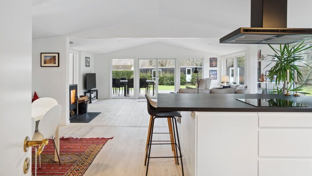 A modern kitchen with a large island, a dining area with a red patterned rug, and a view of the outdoor patio. - Relaxing sanctuary in desirable area (Hornbæk)