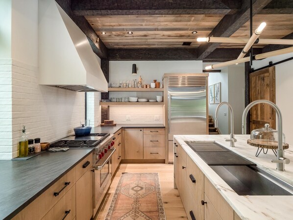 Una cocina moderna con un refrigerador de acero inoxidable, estufa a gas, armarios de madera y encimera de mármol.
