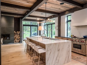 Una cocina moderna con una isla grande, taburetes de bar, estufa integrada y chimenea.