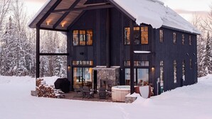 A modern cabin with a large glass door, a stone fireplace, and a hot tub. - Exquisite Rustic Modern Ski Haus Right on MT Abram Bike Park (Greenwood)