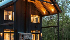 A modern log cabin with a stone fireplace, outdoor seating, and a hot tub. - Exquisite Rustic Modern Ski Haus Right on MT Abram Bike Park (Greenwood)
