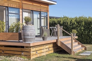 A modern house with a wooden deck, outdoor furniture, and a staircase leading to the entrance.