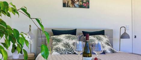 Une chambre à coucher avec un lit, une table de chevet avec une lampe, un tableau accroché au mur et une petite table de nuit avec une plante.