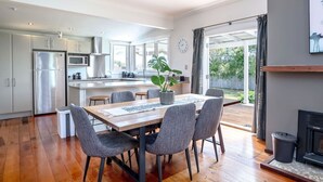 Une cuisine moderne dotée d’appareils électroménagers en acier inoxydable, un coin repas avec une table en bois et des chaises grises, et une grande fenêtre offrant une vue sur l’extérieur.
