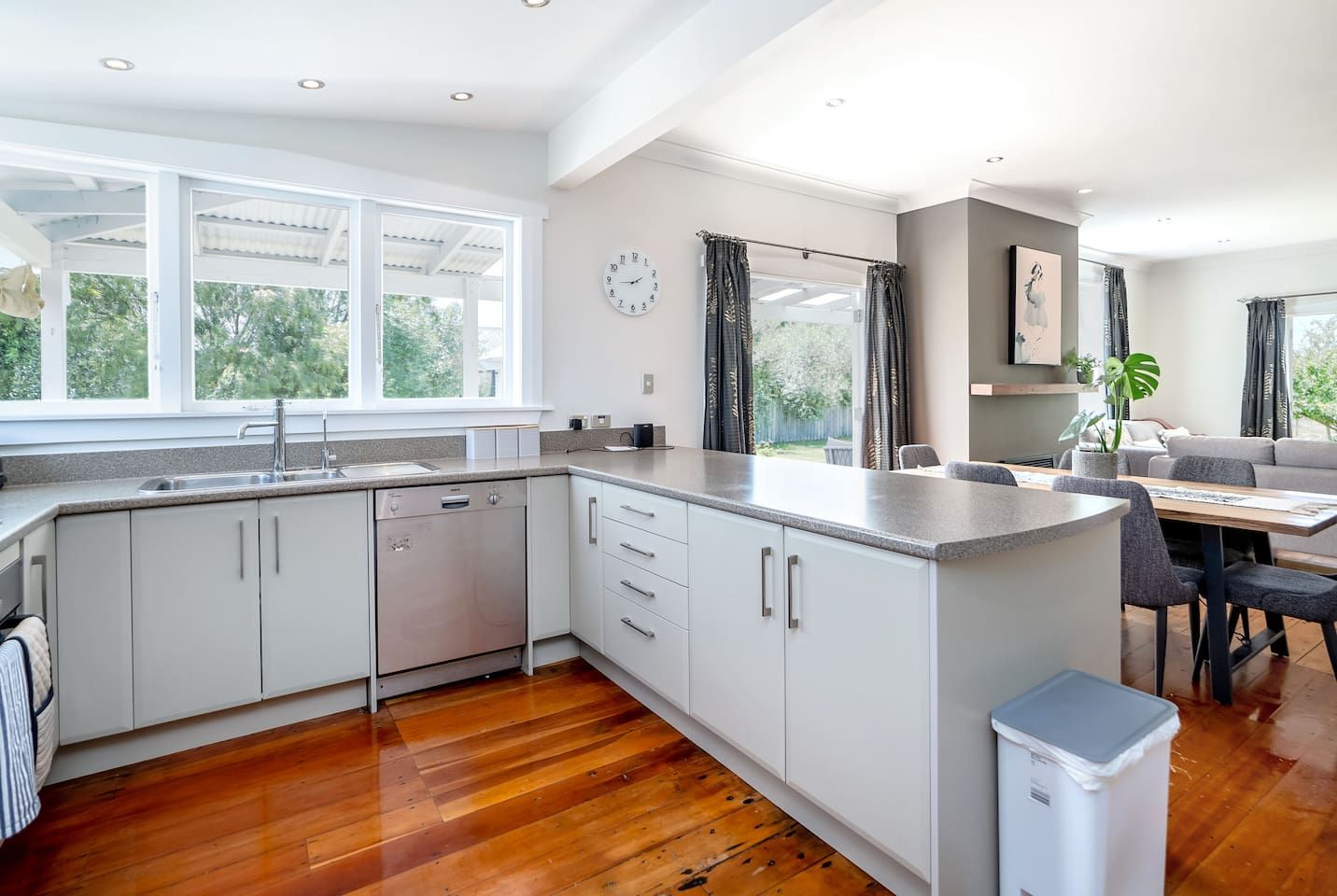 A modern kitchen with white cabinetry, a built-in dishwasher, and a dining area with a table and chairs.