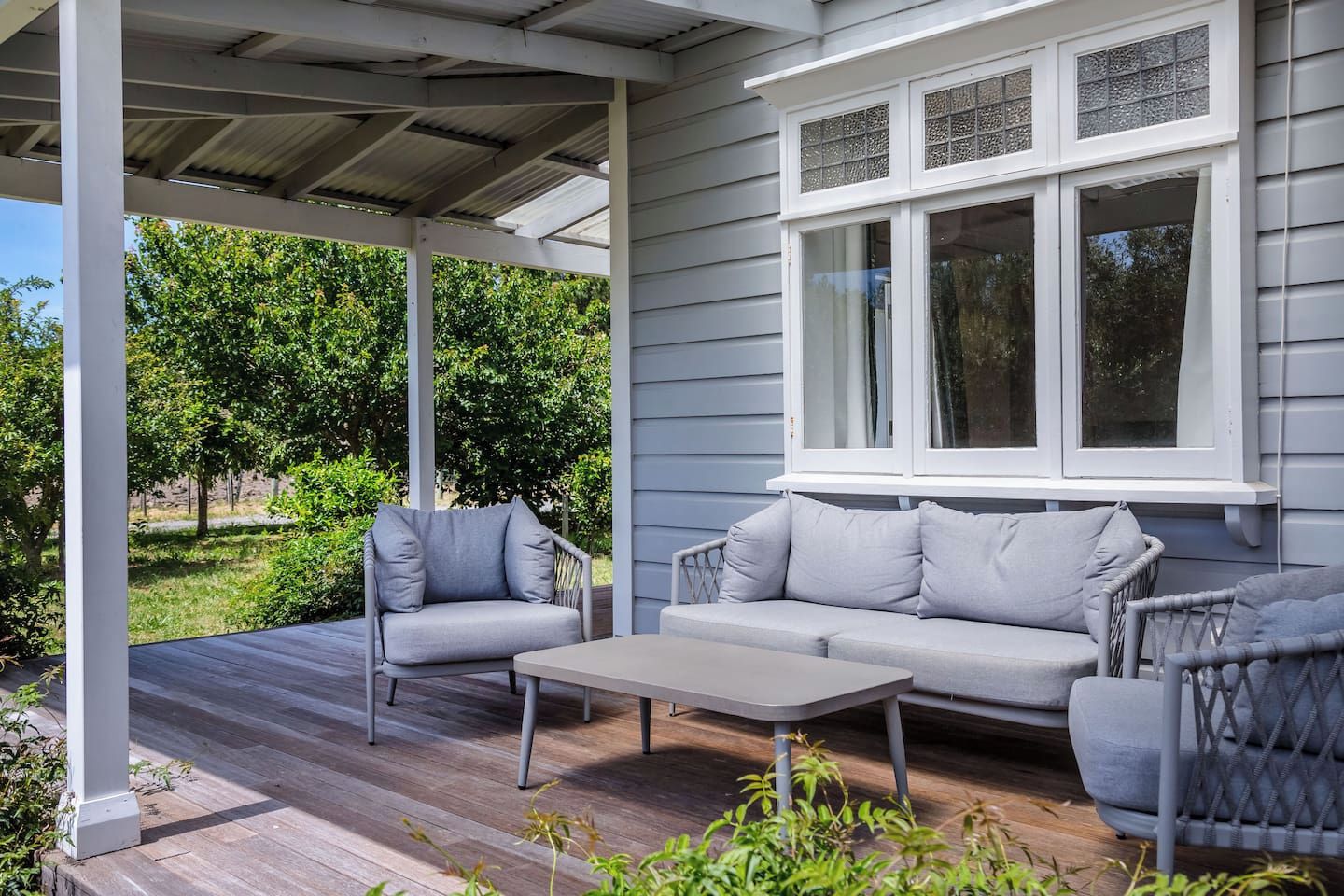 A covered porch with a grey sofa, a small table, and wicker chairs.