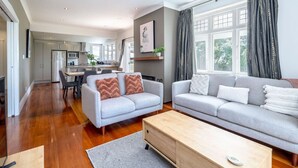 Un salon moderne avec un canapé gris, une table basse en bois et un coin repas, la cuisine étant visible au fond.