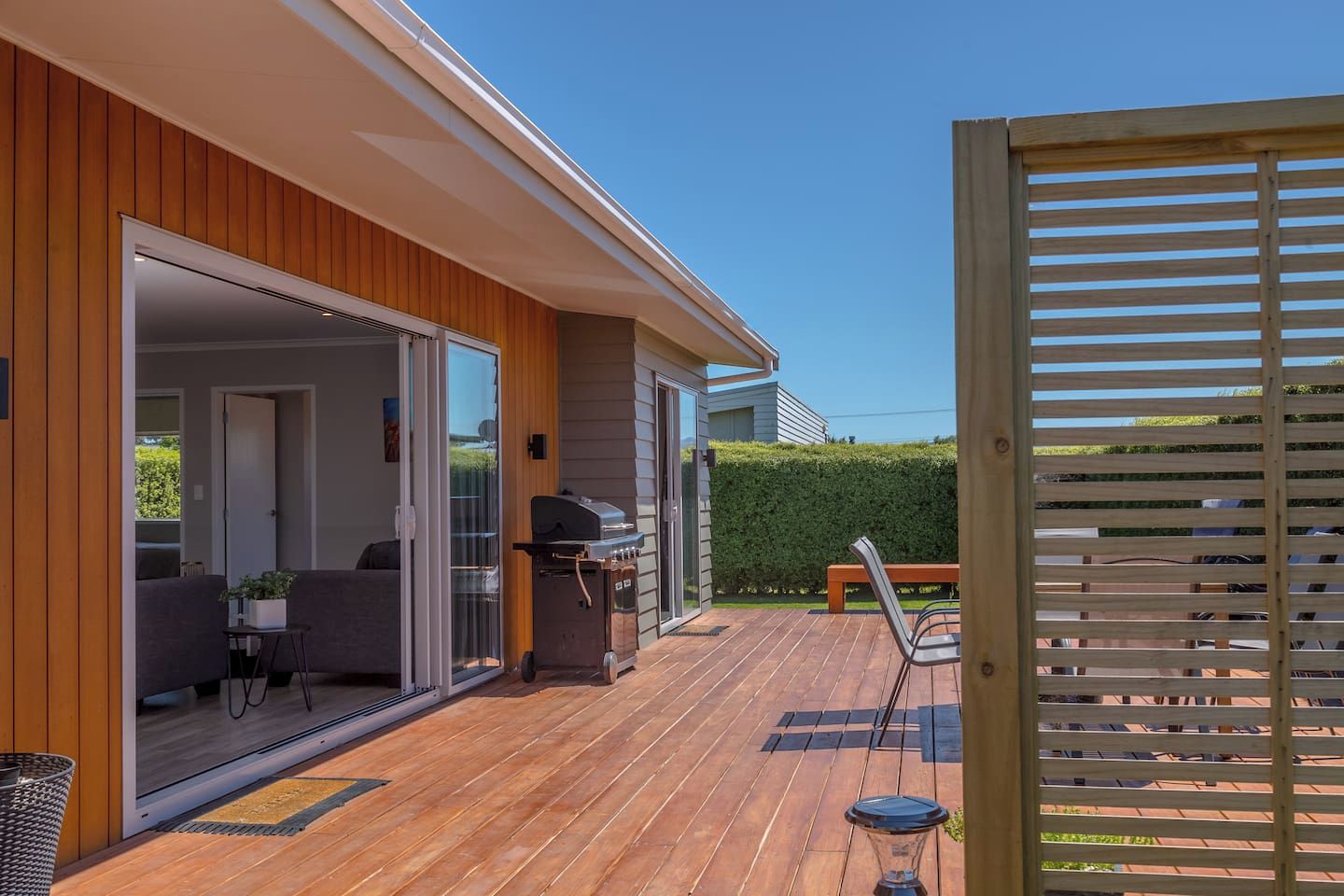 A wooden deck with a barbecue grill, outdoor seating, and a view of a neighboring property.