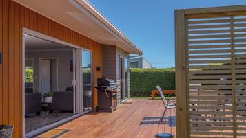 A wooden deck with a barbecue grill, outdoor seating, and a view of a neighboring property.