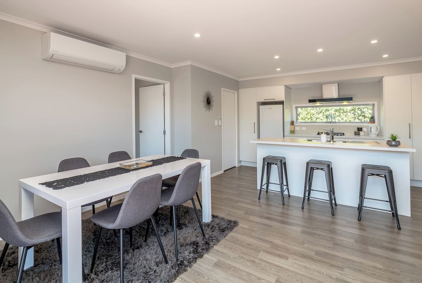 A modern kitchen with a central island, bar stools, and a dining area with a table and chairs.