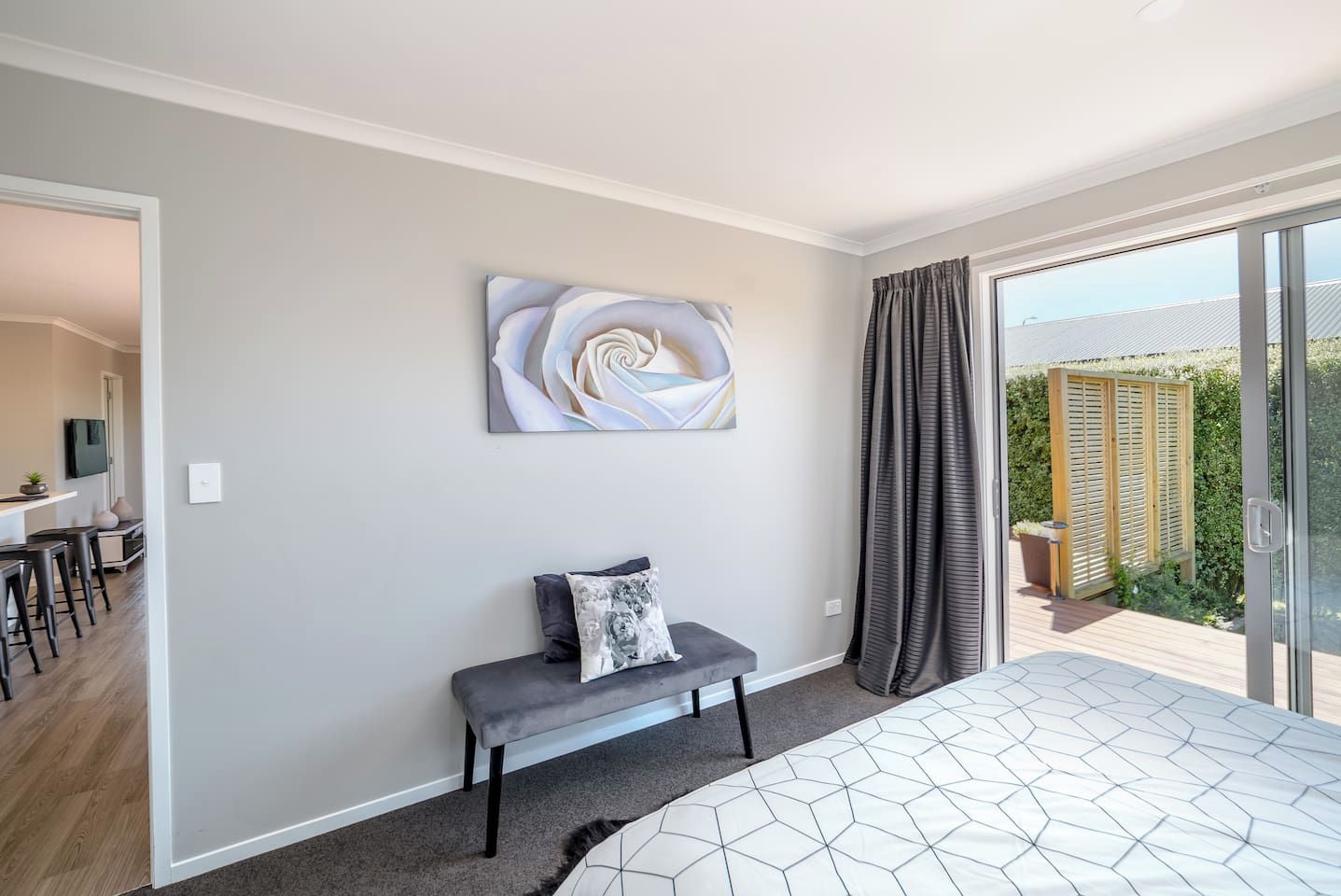 A bedroom with a bed, a bench, a wall-mounted artwork, and a view of a garden through a sliding door.