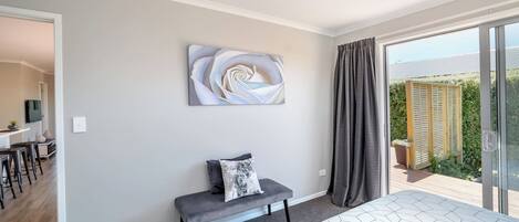 A bedroom with a bed, a bench, a wall-mounted artwork, and a view of a garden through a sliding door.