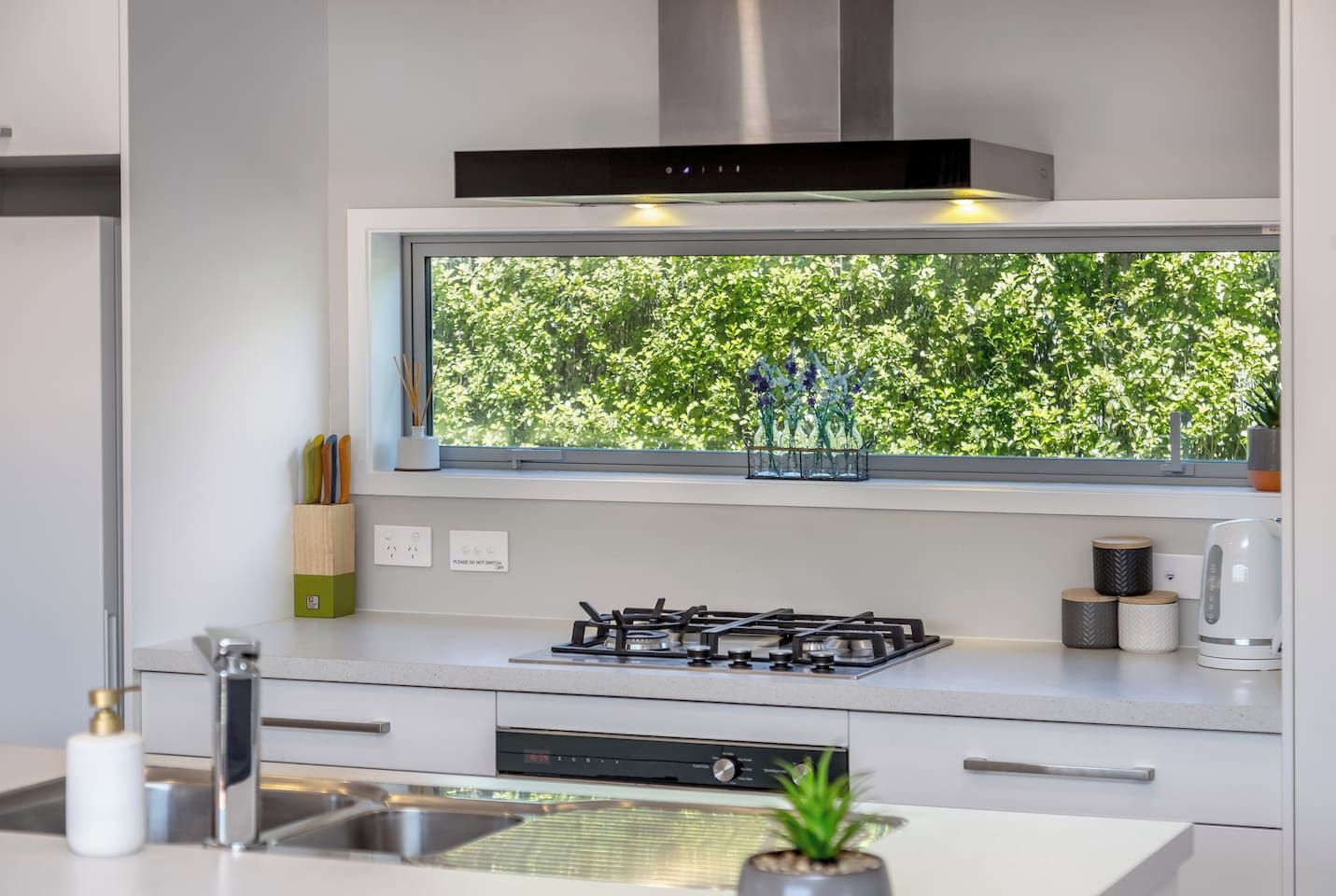 A modern kitchen with a built-in gas stove, a window with a view of greenery, and a kettle on the counter.